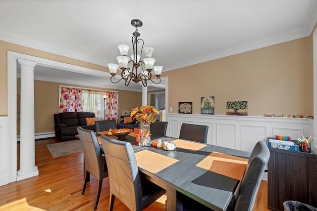 dining room with a baseboard heating unit, ornate columns, light wood-type flooring, ornamental molding, and a notable chandelier