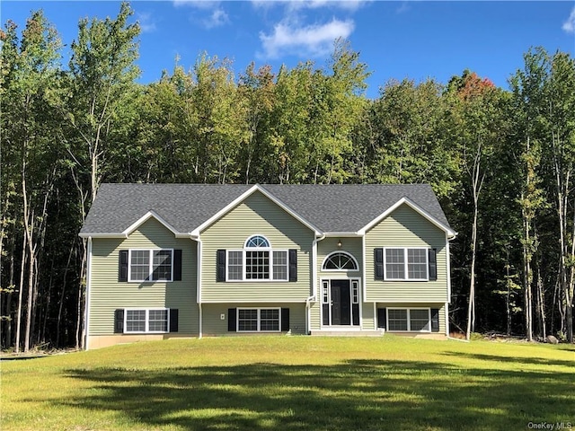 bi-level home with a front yard, a forest view, and roof with shingles