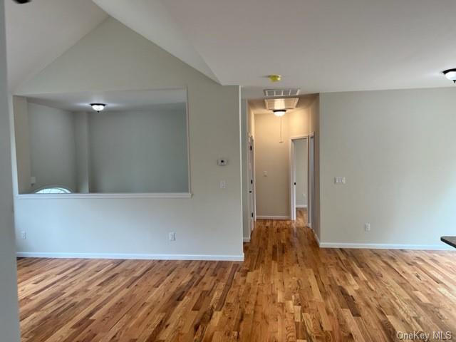 unfurnished room with lofted ceiling, wood finished floors, visible vents, and baseboards