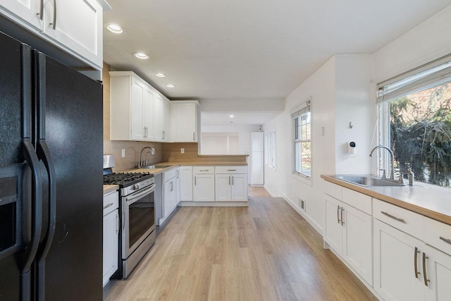 kitchen with stainless steel gas stove, white cabinetry, black fridge, and sink