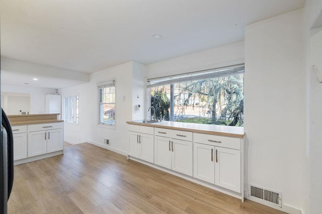 kitchen with white cabinets, light wood-type flooring, and sink