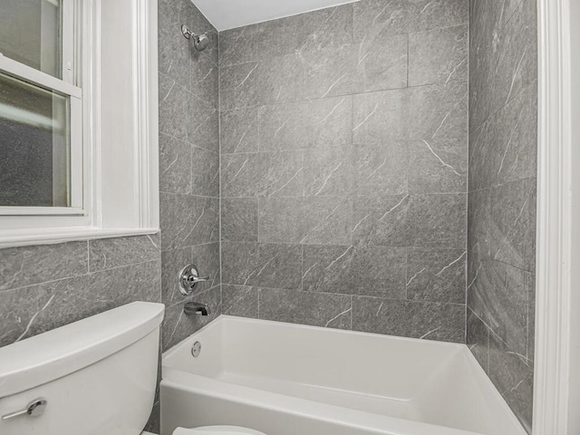 bathroom with toilet, tiled shower / bath, and tile walls