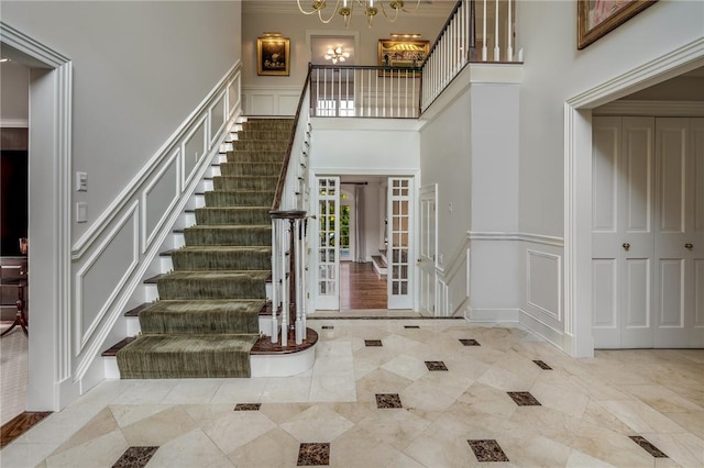 foyer with french doors, a towering ceiling, ornamental molding, and a notable chandelier