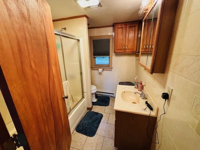 full bathroom featuring vanity, shower / bath combination with glass door, a baseboard heating unit, toilet, and tile walls