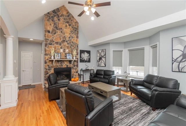 living room featuring high vaulted ceiling, a stone fireplace, ceiling fan, light hardwood / wood-style floors, and decorative columns