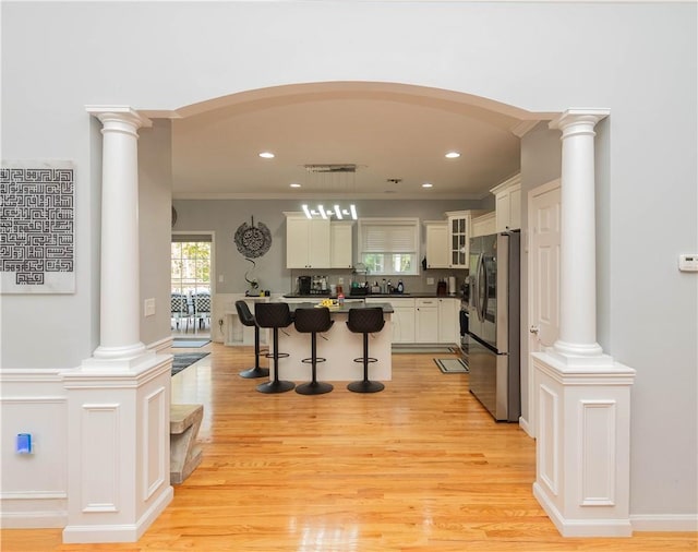 kitchen featuring stainless steel fridge, white cabinets, a center island, light hardwood / wood-style floors, and a breakfast bar area