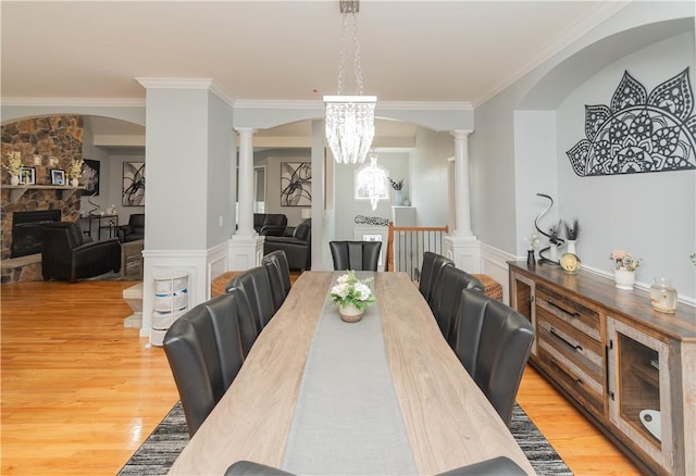 dining space featuring a notable chandelier, light hardwood / wood-style floors, a stone fireplace, and crown molding