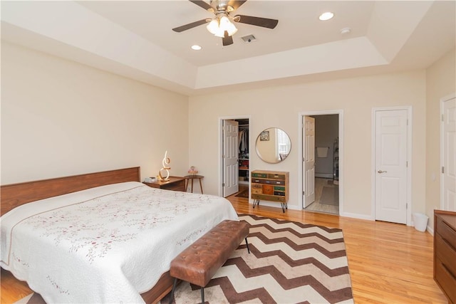 bedroom featuring a raised ceiling, connected bathroom, light hardwood / wood-style flooring, and ceiling fan