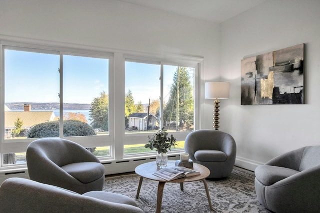 sitting room with hardwood / wood-style flooring, a baseboard heating unit, and a water view