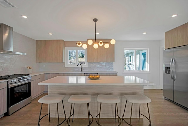 kitchen with sink, a kitchen island, stainless steel appliances, and wall chimney range hood