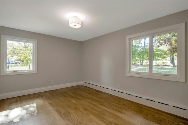 empty room with light hardwood / wood-style floors, a wealth of natural light, and a baseboard radiator