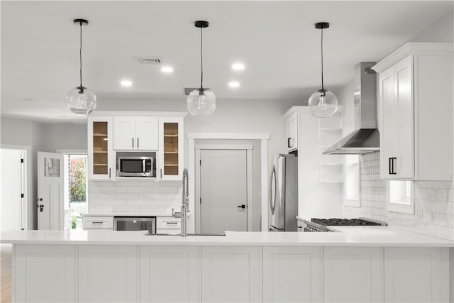 kitchen featuring pendant lighting, wall chimney range hood, tasteful backsplash, white cabinetry, and stainless steel appliances