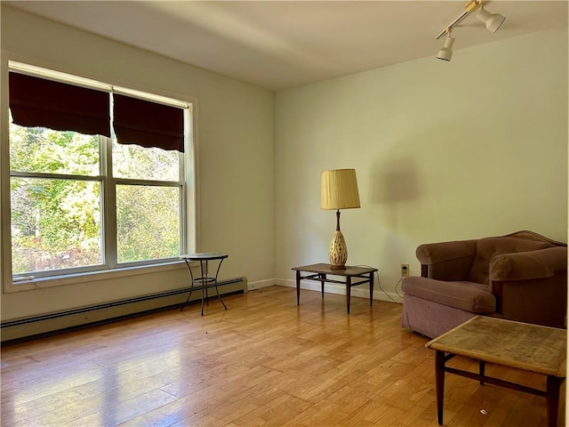 living area featuring rail lighting, light hardwood / wood-style floors, and a baseboard heating unit