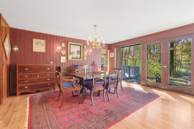 dining space featuring a chandelier, french doors, light hardwood / wood-style floors, and wooden walls