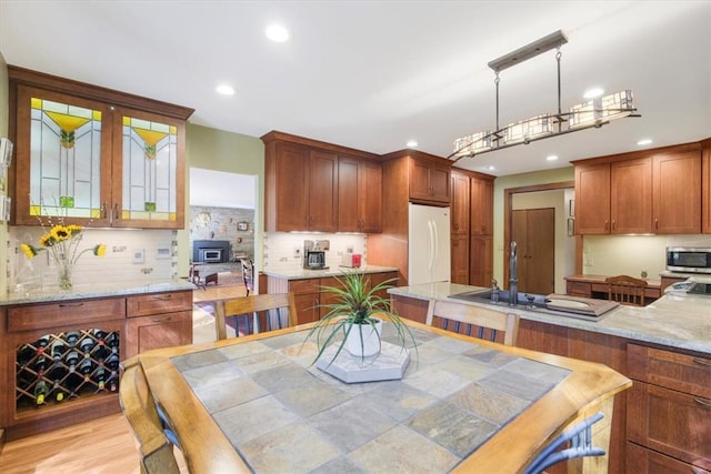 kitchen with decorative backsplash, light wood-type flooring, decorative light fixtures, white fridge, and light stone counters