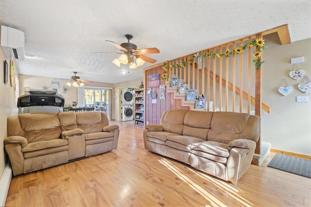 living room with a textured ceiling, hardwood / wood-style flooring, stacked washer / dryer, and ceiling fan