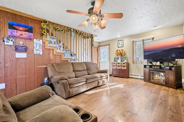 living room with ceiling fan, baseboard heating, wood walls, a textured ceiling, and hardwood / wood-style flooring