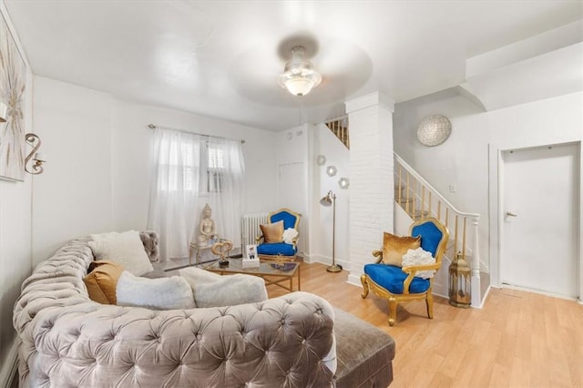 living area with light wood-type flooring, ornate columns, radiator, and ceiling fan