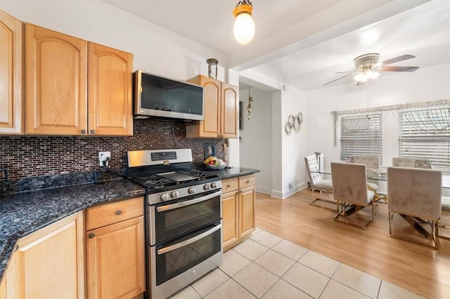 kitchen featuring ceiling fan, stainless steel appliances, dark stone countertops, light hardwood / wood-style floors, and decorative backsplash