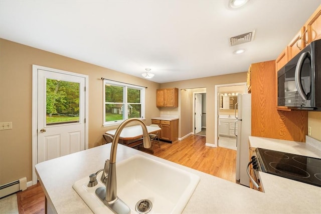 kitchen featuring white appliances, light hardwood / wood-style floors, baseboard heating, and sink