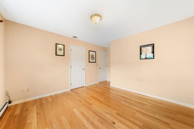 empty room featuring a baseboard radiator and light hardwood / wood-style flooring