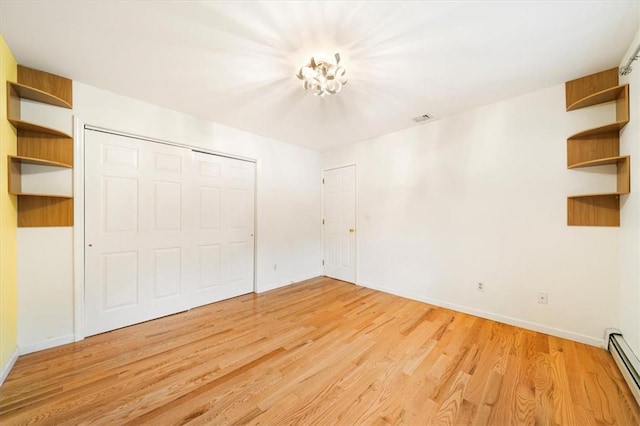 unfurnished bedroom featuring light wood-type flooring, a closet, and baseboard heating