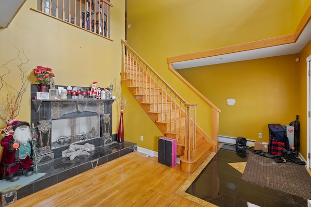 living room with a tiled fireplace, baseboards, wood finished floors, stairway, and a baseboard radiator