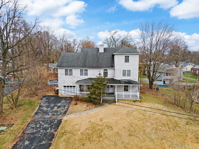 view of front of home with a front lawn, a porch, a chimney, an attached garage, and aphalt driveway