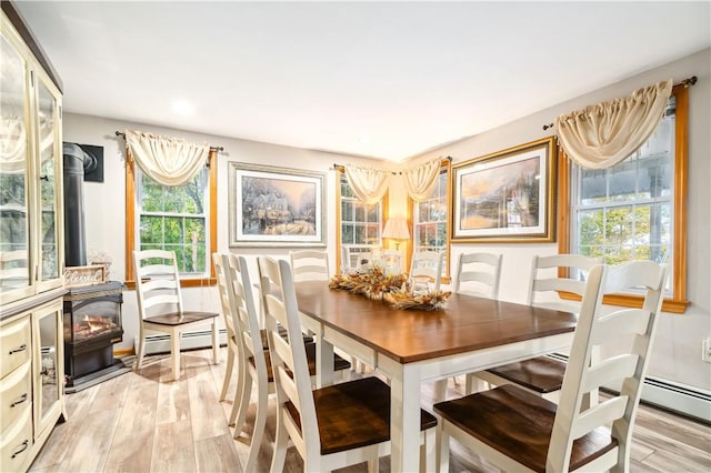 dining area with light wood-type flooring, a baseboard radiator, and a wood stove