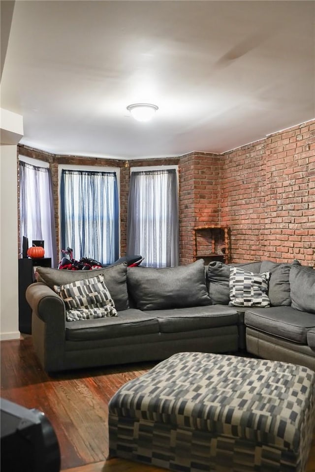 living room featuring a fireplace, dark wood-type flooring, and brick wall