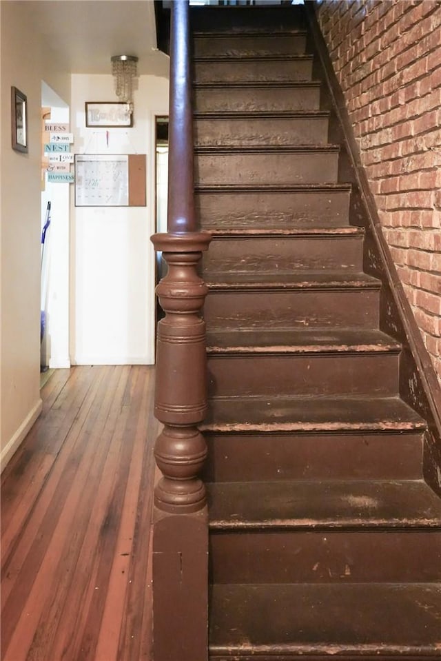 stairs with hardwood / wood-style floors and brick wall