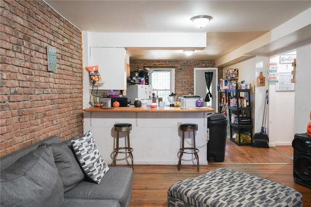 interior space featuring kitchen peninsula, a kitchen breakfast bar, wood-type flooring, and brick wall