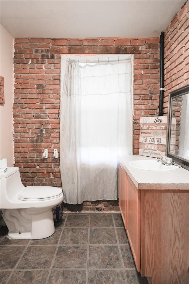 bathroom featuring vanity, brick wall, and toilet