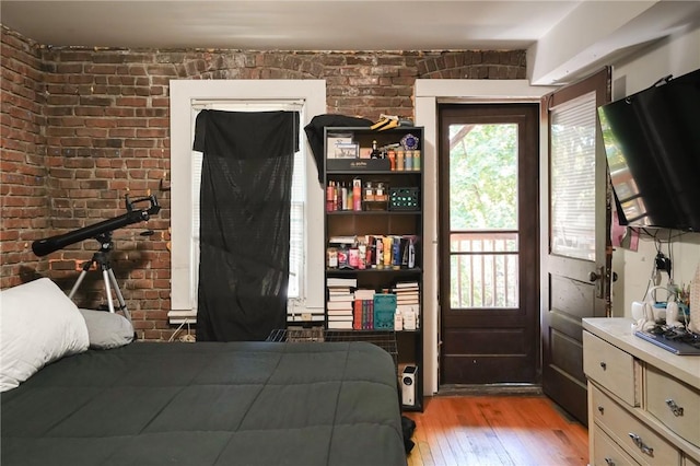 bedroom with light wood-type flooring and brick wall