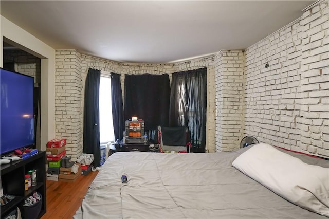 bedroom with hardwood / wood-style flooring and brick wall