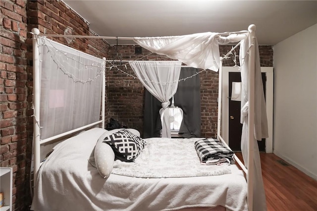 bedroom with wood-type flooring and brick wall