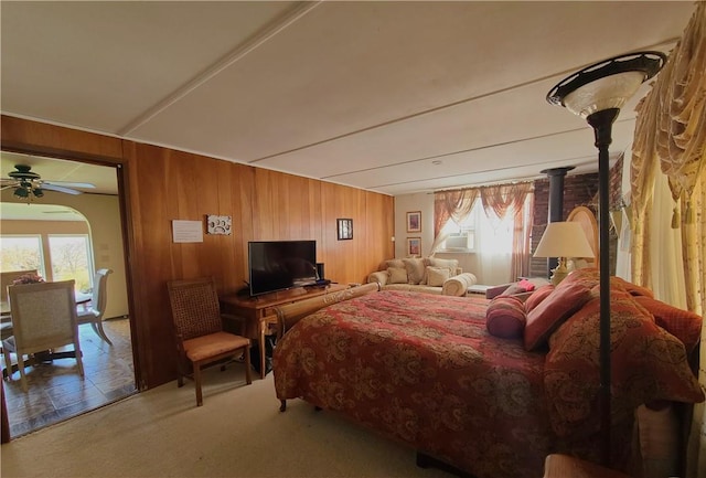 bedroom featuring carpet flooring, a wood stove, wooden walls, and multiple windows