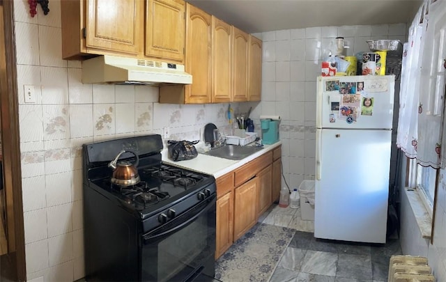 kitchen with gas stove, white fridge, tile walls, and sink