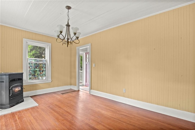 unfurnished living room featuring a chandelier, wood-type flooring, a wood stove, and crown molding