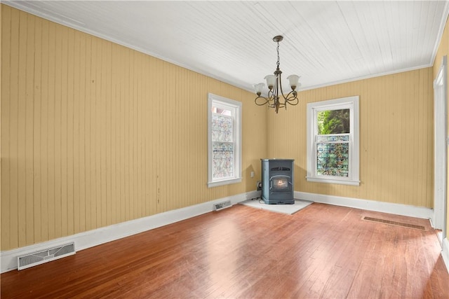 empty room with a wood stove, an inviting chandelier, crown molding, wooden walls, and hardwood / wood-style flooring