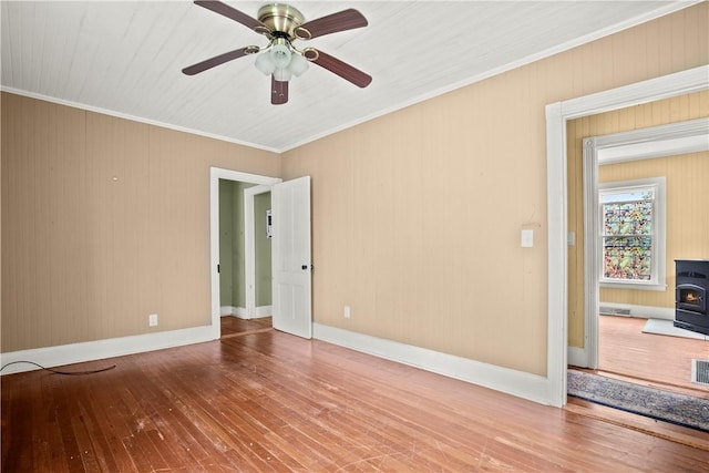 unfurnished room featuring hardwood / wood-style floors, a wood stove, ceiling fan, and ornamental molding