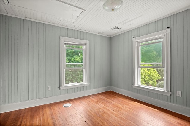 empty room with hardwood / wood-style floors, wooden walls, and a wealth of natural light