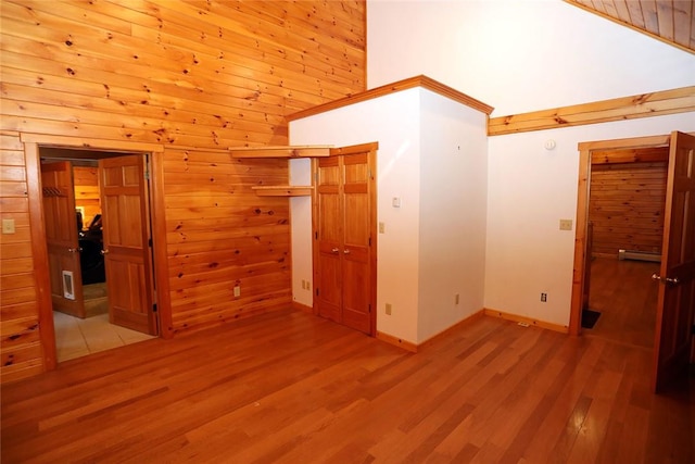 unfurnished bedroom featuring wood walls, a closet, high vaulted ceiling, and light wood-type flooring