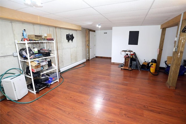 basement featuring baseboard heating, electric panel, hardwood / wood-style floors, and a drop ceiling