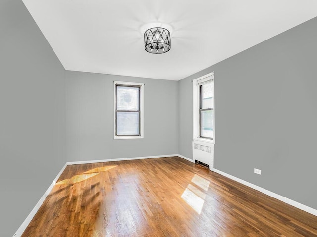 empty room featuring radiator heating unit, an inviting chandelier, and wood-type flooring