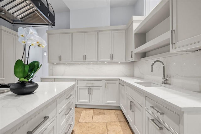 kitchen with white cabinetry, sink, wall chimney range hood, light stone counters, and backsplash