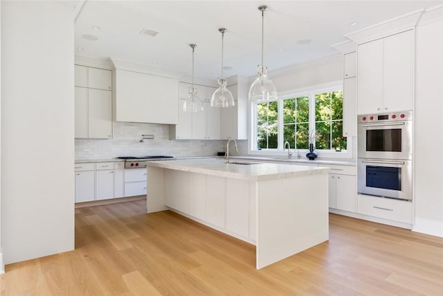 kitchen featuring white cabinetry, stainless steel appliances, sink, hanging light fixtures, and a center island with sink