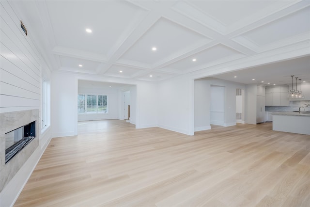 unfurnished living room featuring coffered ceiling, light wood-type flooring, a high end fireplace, beam ceiling, and sink