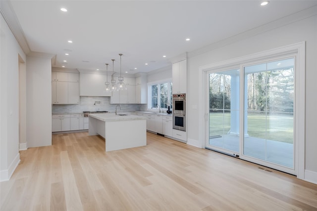 kitchen with pendant lighting, white cabinetry, sink, a kitchen island with sink, and light hardwood / wood-style flooring