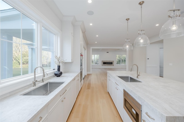 kitchen with decorative light fixtures, sink, light stone counters, and white cabinets